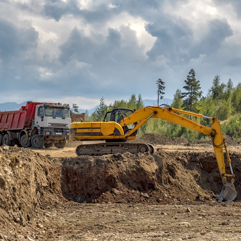 Yellow excavator and empty truck working at the construction site